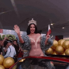 a woman with a crown on her head is standing in front of gold balloons