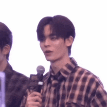 a young man in a plaid shirt is holding a microphone and talking into it .
