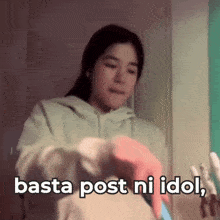 a woman in a green hoodie is holding a cell phone with the words basta post ni idol below her