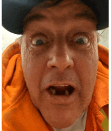 a man wearing a hat and an orange hoodie makes a funny face