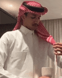 a man wearing a white shirt and a red and white scarf is holding a cup of coffee .