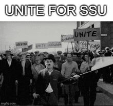 a black and white photo of a crowd of people marching down a street holding signs .