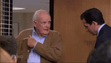 a man in a suit and tie is talking to an older man in a brown sweater .