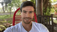 a man in a white shirt smiles while sitting in a red chair