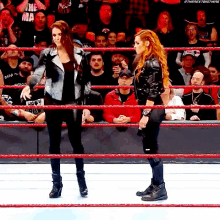 two women are standing in a wrestling ring with a crowd behind them .