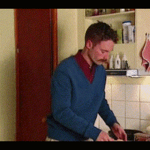 a man in a blue sweater stands in a kitchen