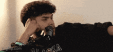 a man wearing a black alaska shirt is talking into a microphone .
