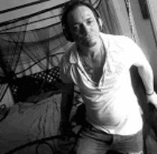 a man wearing headphones and a white shirt is standing in front of a bed .