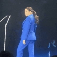 a woman in a blue suit stands on a stage in front of a microphone .