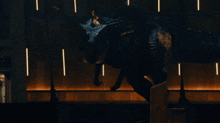 a large black dinosaur is standing in a dark room with lights behind it