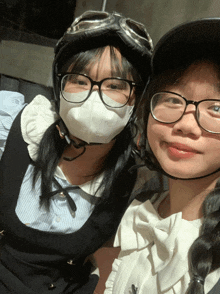 a girl wearing glasses and a helmet stands next to another girl wearing a mask
