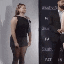 a woman in a black dress is standing next to a man in a suit in front of a sign that says slushy