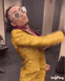 a man in a yellow suit and sunglasses is dancing in a room .