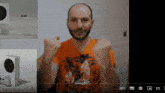 a man in an orange shirt holds his fist in the air in front of a white box that says $ 299