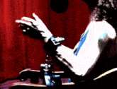 a person is sitting in front of a red curtain with their hands outstretched