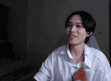 a young man wearing headphones and a white shirt smiles in a dark room