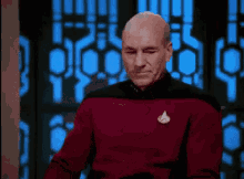a bald man is wearing a red sweater with a star trek logo on it .