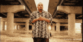 a man wearing a shirt that says ' hawaii ' on it is standing under a bridge