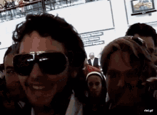 a man wearing sunglasses is smiling in front of a sign that says rbd.gif