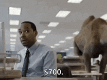 a man in a suit and tie is sitting at a desk in front of a computer while an elephant walks past him .