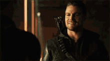 a man in a green arrow suit is smiling while holding an arrow .