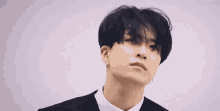 a young man with black hair and a white shirt is wearing a black suit and earrings .