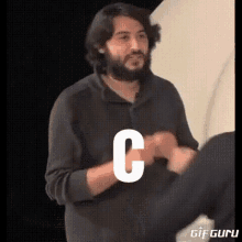 a man with a beard is giving a fist bump with the letter c on his chest .