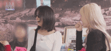 two women are laughing in front of a sign that says 123 ive5