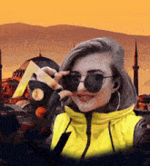 a woman wearing sunglasses and a yellow jacket is holding a piece of paper in front of a mosque