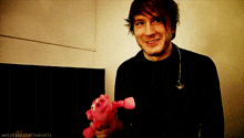 a man in a black shirt is smiling while holding a pink stuffed pig