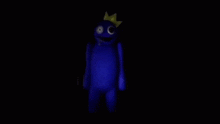 a blue stuffed animal with a yellow crown on its head is standing in the dark .