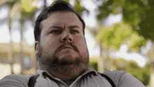 a man with a beard and suspenders is looking at the camera with a serious look on his face .