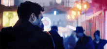 a man in a mask is standing in a crowd of people in a city at night .