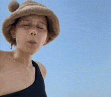 a woman wearing a hat and a black tank top looks at the camera