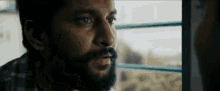 a man with a beard is looking out a window on a train .