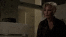 a woman is standing in a dark room in front of a refrigerator in a kitchen .