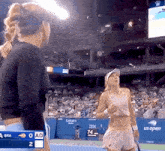 two women are standing on a tennis court with a scoreboard that says us open in the background