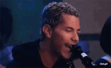 a man is singing into a microphone and smiling while playing a guitar .