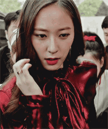 a woman wearing a red top with a bow around her neck looks at the camera
