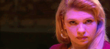 a close up of a woman 's face in a dark room with purple lights behind her .