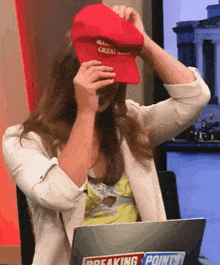 a woman covering her face with a red hat that says make america great