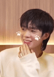 a young man with paw prints on his face is smiling and covering his mouth with his hand .