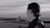 a black and white photo of a man in a leather jacket standing on a rooftop overlooking a city .