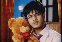 a man wearing glasses holds a teddy bear with a red bow