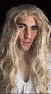 a man with long blonde hair and blue eyes wearing a white shirt