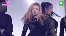 a woman is singing into a microphone while a group of women are dancing in front of her .