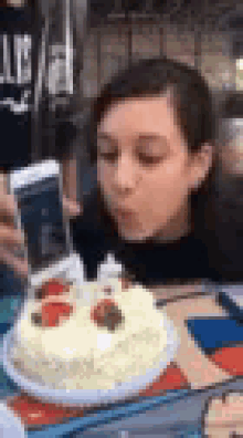 a woman is blowing out a candle on a birthday cake while taking a selfie with her phone .