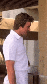 a man in a white shirt and white pants is standing next to a wall .