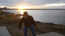 a man standing on the shore of a body of water with the sun setting in the background
