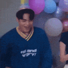 a man wearing a party hat stands in front of a wall of balloons and a woman